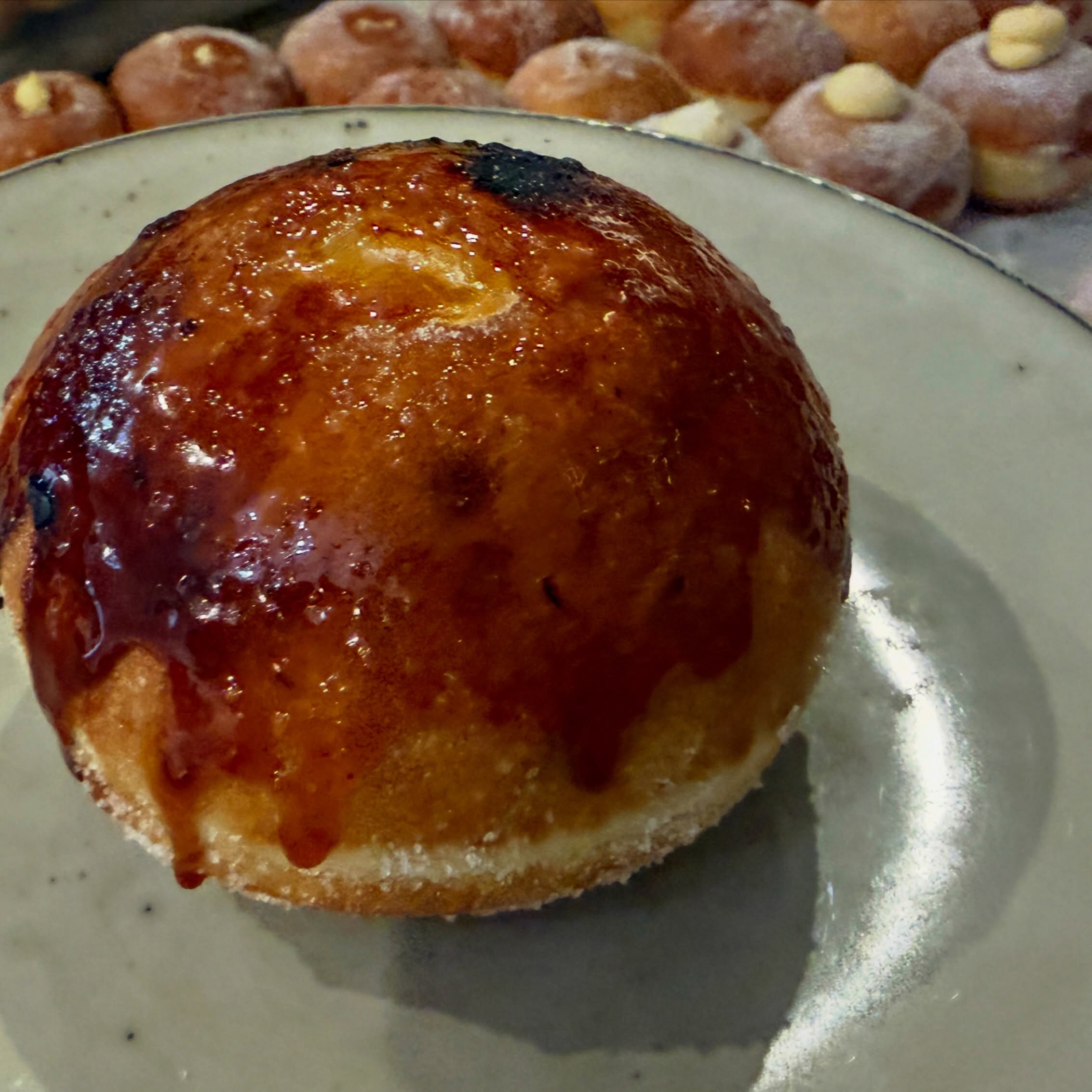A doughnut with a caramelised brûlée top, with a tray of sugared doughnuts behind