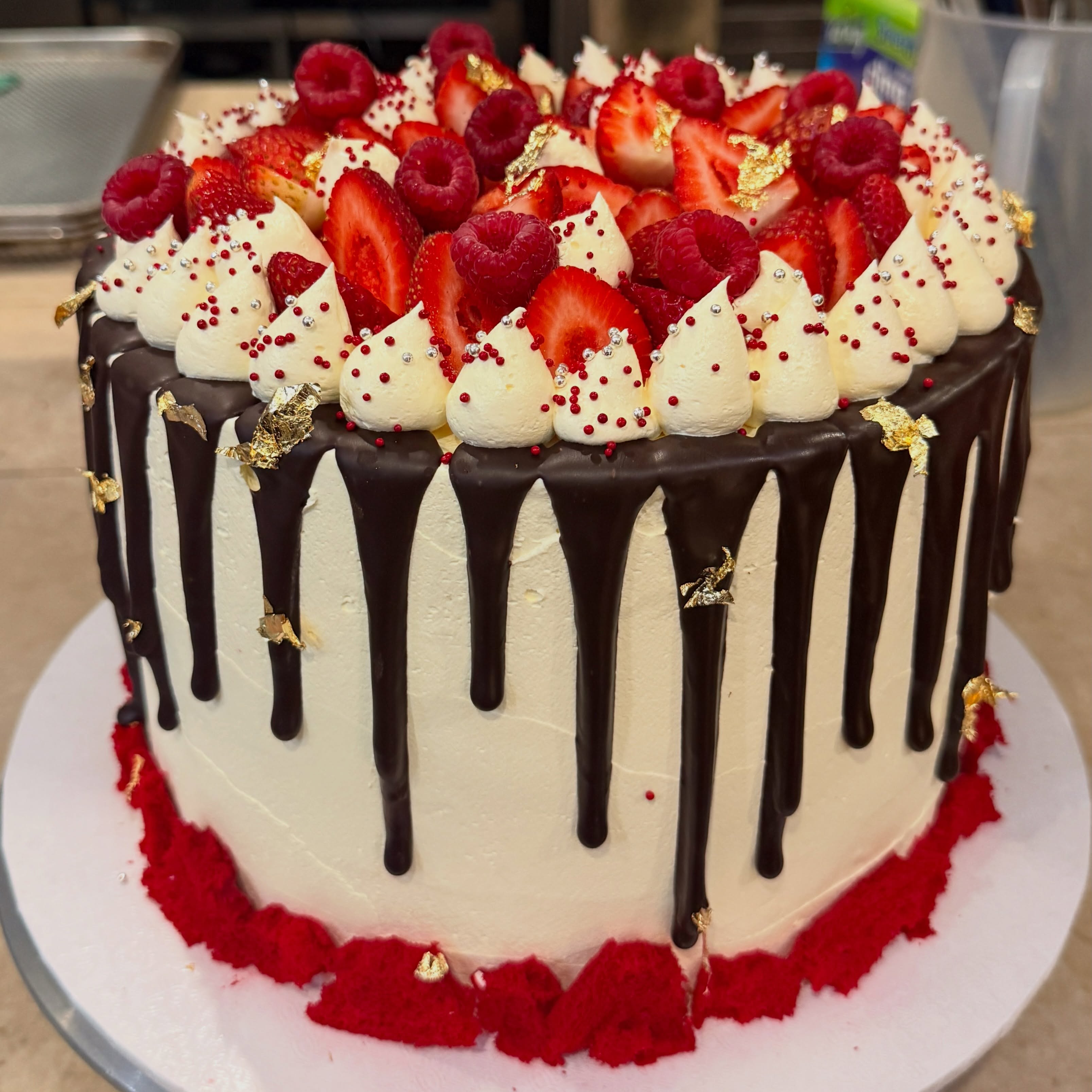 Dark chocolate drip cake topped with strawberries, raspberries and gold leaf