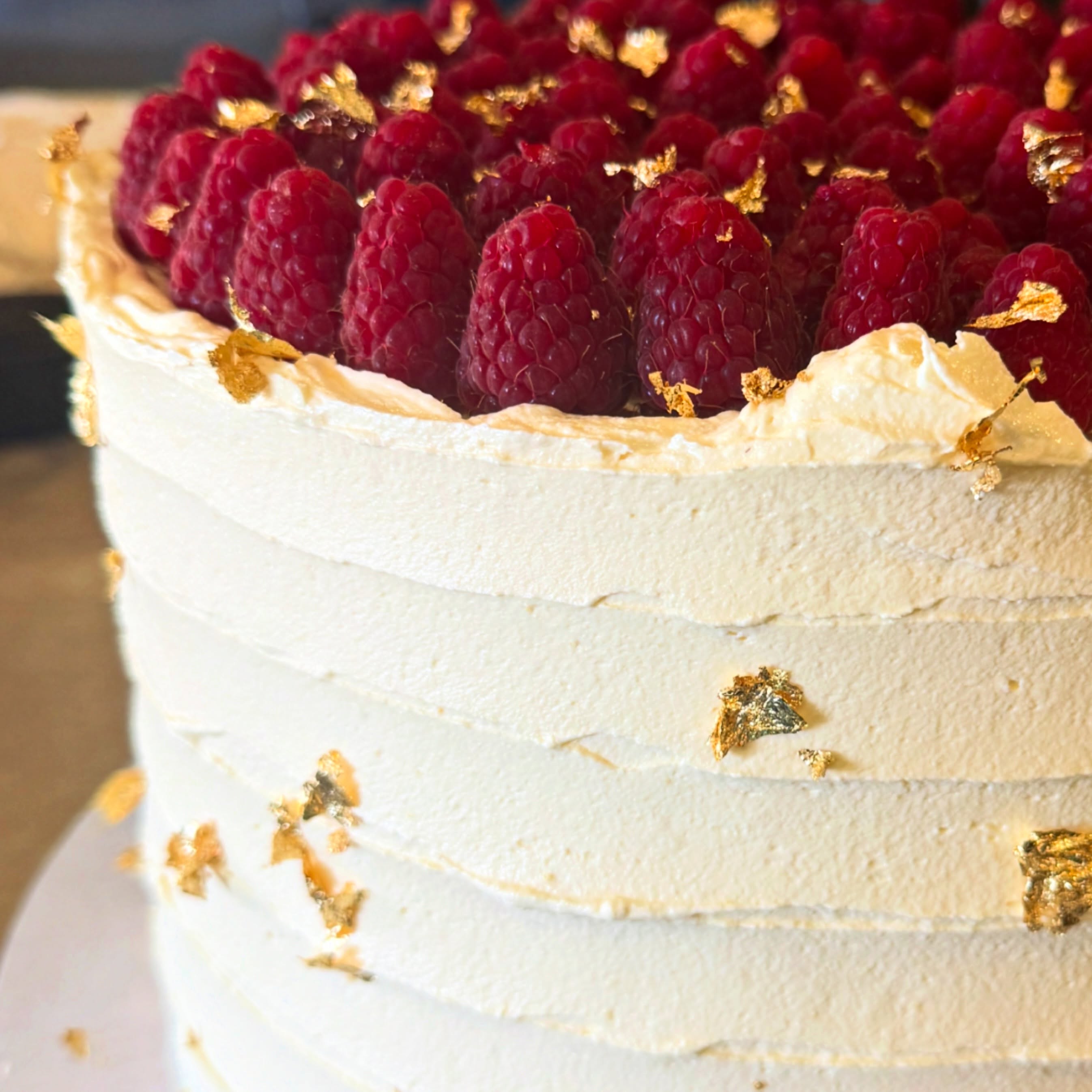 Cream cake topped with fresh raspberries and gold leaf