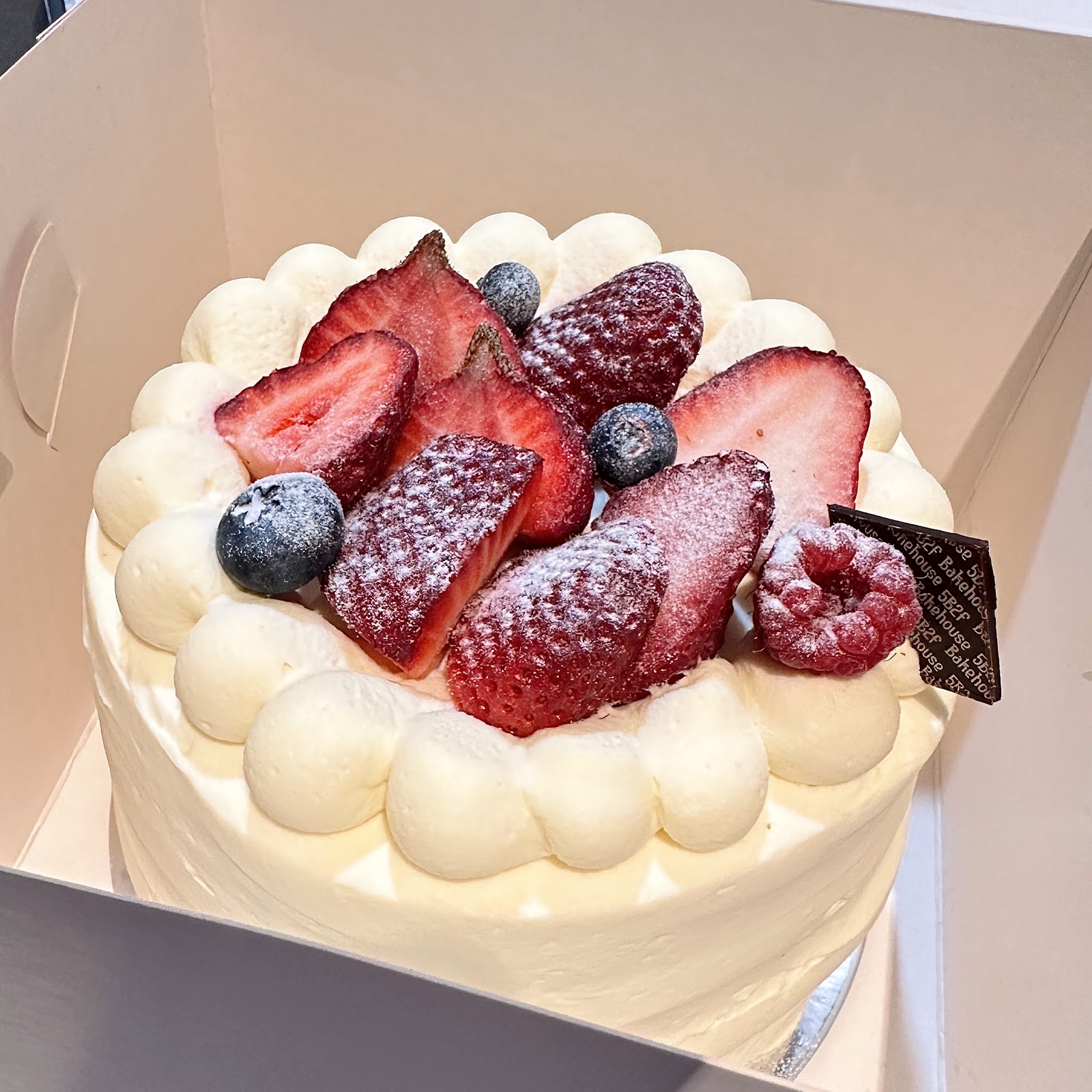 Whole strawberry cream cake in its box, with a 5B2F Bakehouse chocolate plaque