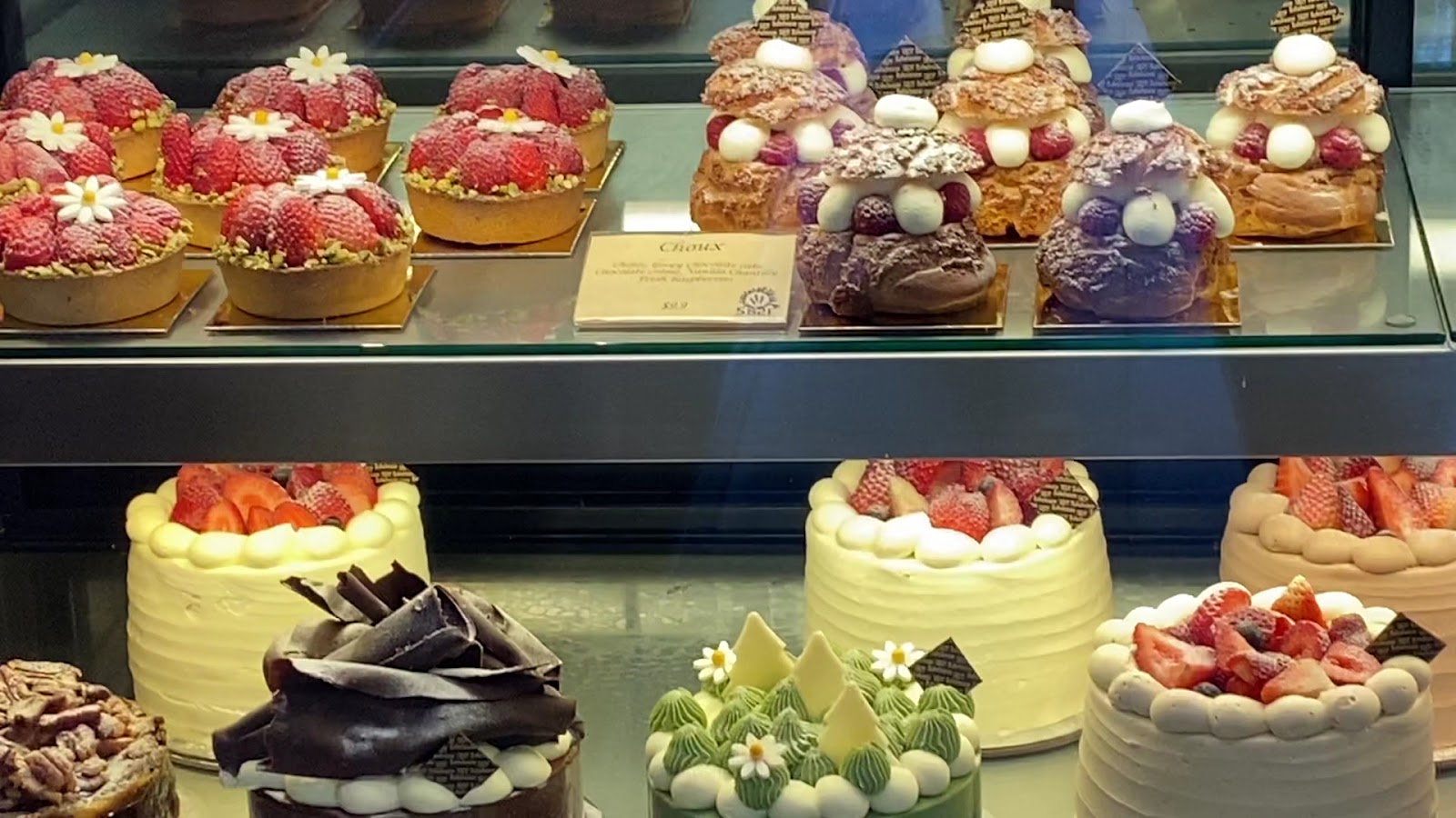 Strawberry tarts, choux buns and cream cakes on the cabinet shelves