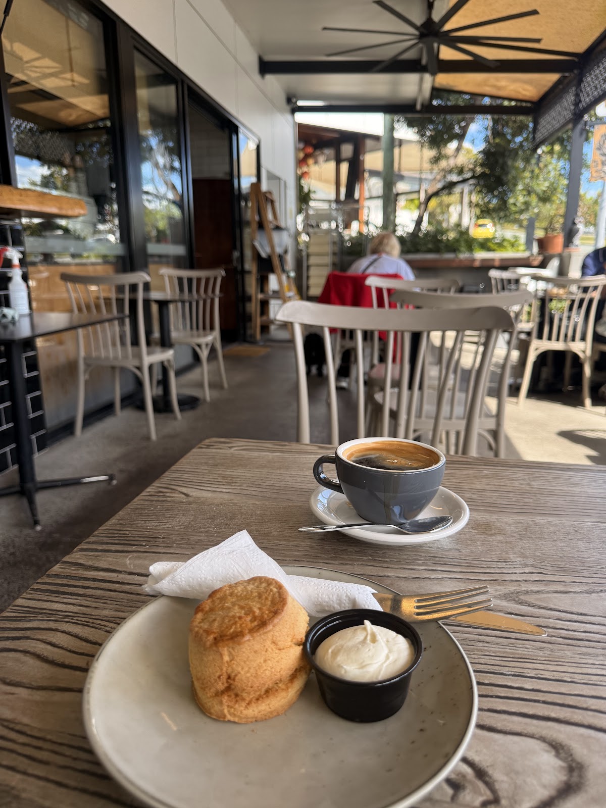 Coffee and a scone with cream at a table under the awning outside the bakehouse