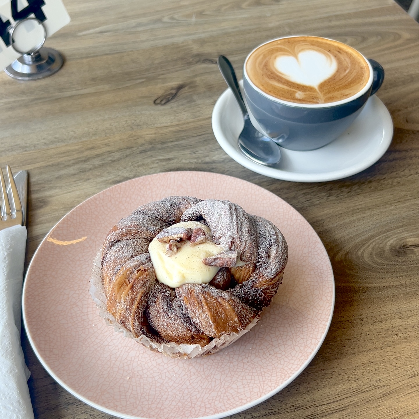 A cruffin with custard and pecans beside a cappuccino