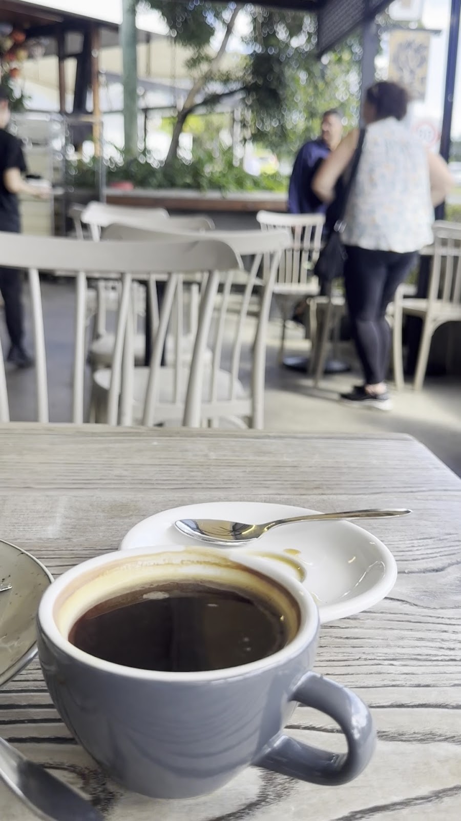 A long black on an outdoor table, with the cafe chairs behind