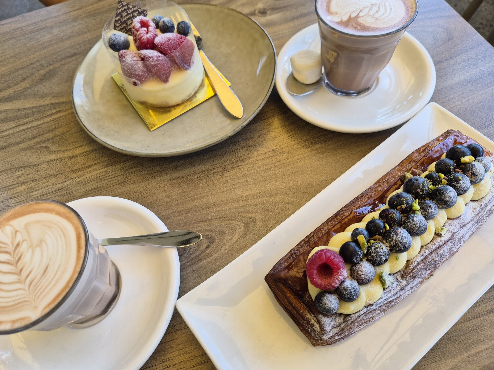 A slice of strawberry cheesecake, a hot chocolate and a blueberry mille-feuille